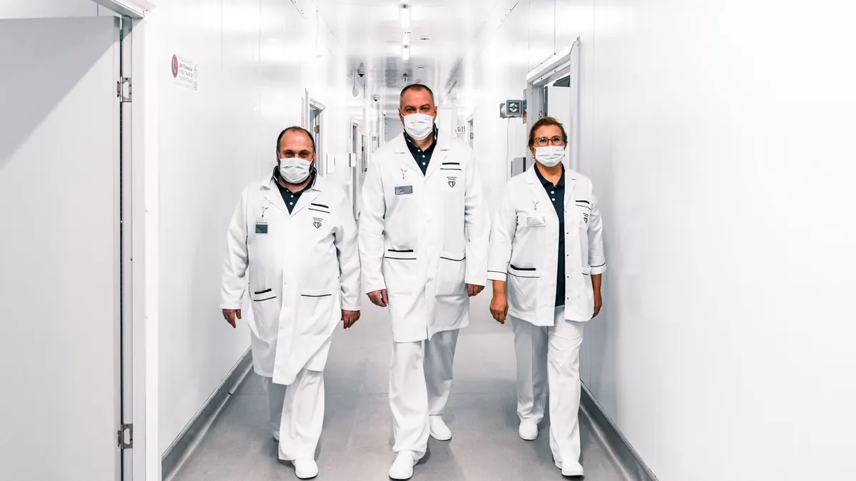 Three clinicians in white coats and masks walking through a bright clinic corridor