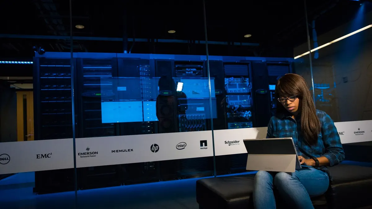 IT professional working on a laptop in front of a glass-walled server room